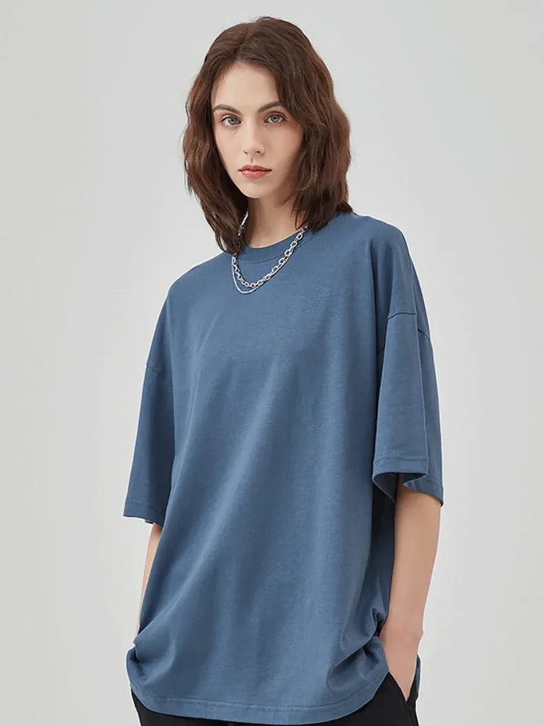 A person with shoulder-length brown hair wears a Custom Anime Character Steel Blue T-Shirt (230GSM 100% cotton), paired with a silver chain necklace and black pants, standing against a plain light background.