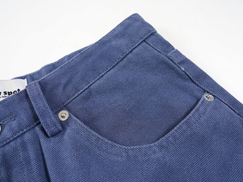 Close-up of blue jorts back waistband and top pocket edge with metal rivets and woven texture