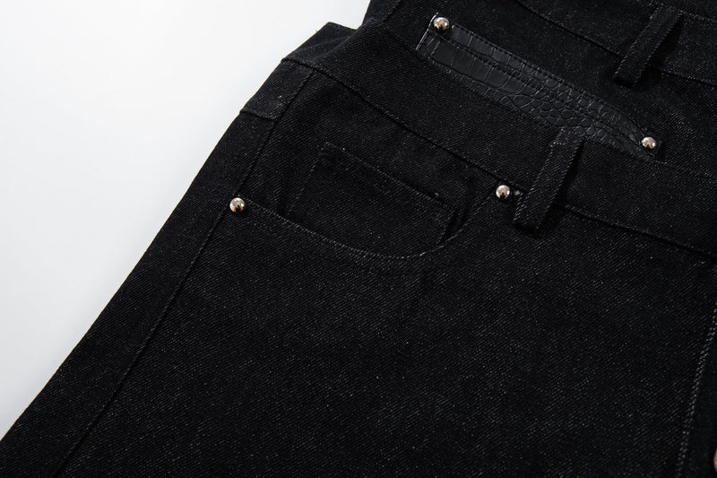Close-up of black denim front pocket area with faux crocodile trim and metal rivets