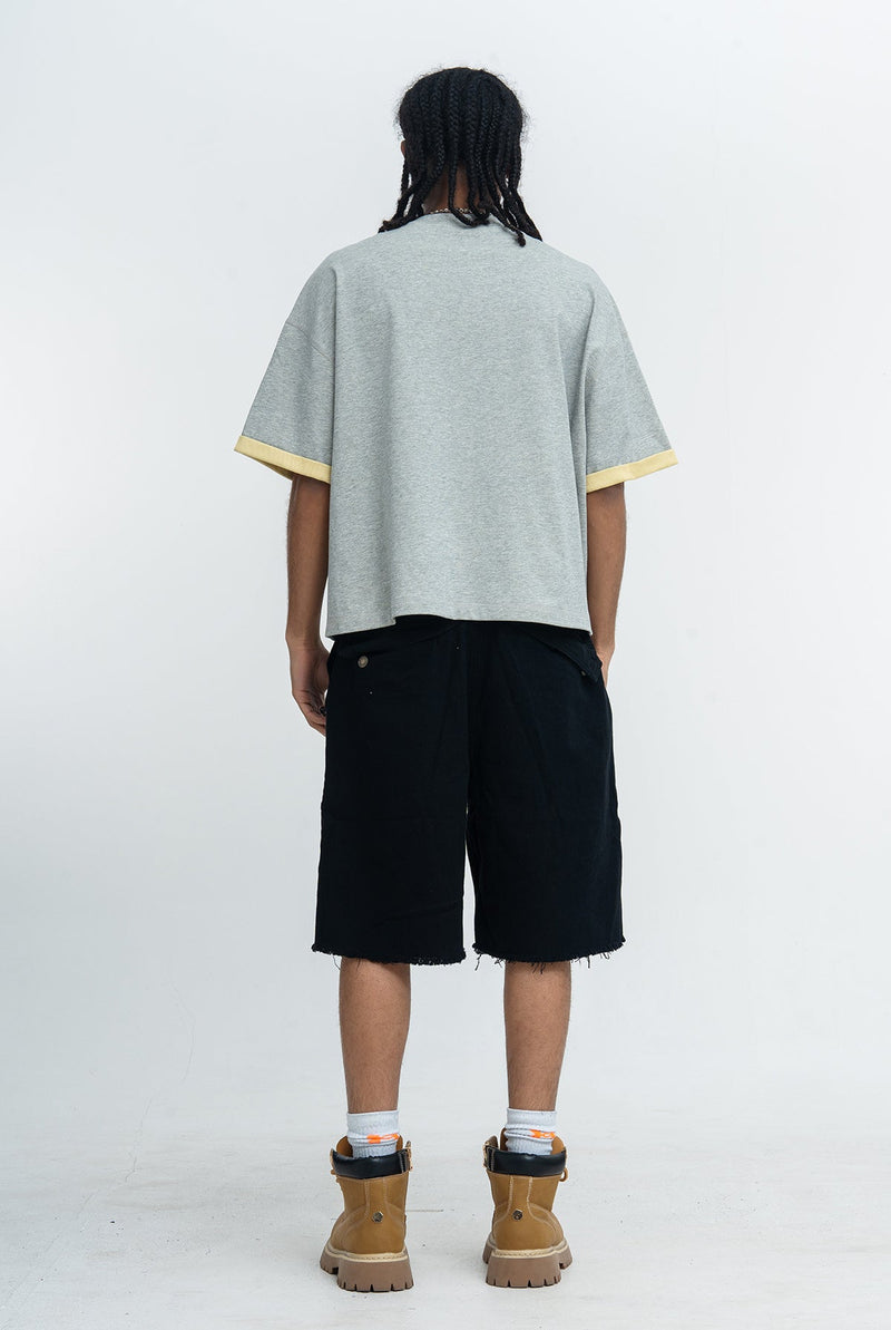 Back view of oversized heather gray varsity graphic tee with yellow sleeve cuffs, styled with black shorts and tan boots