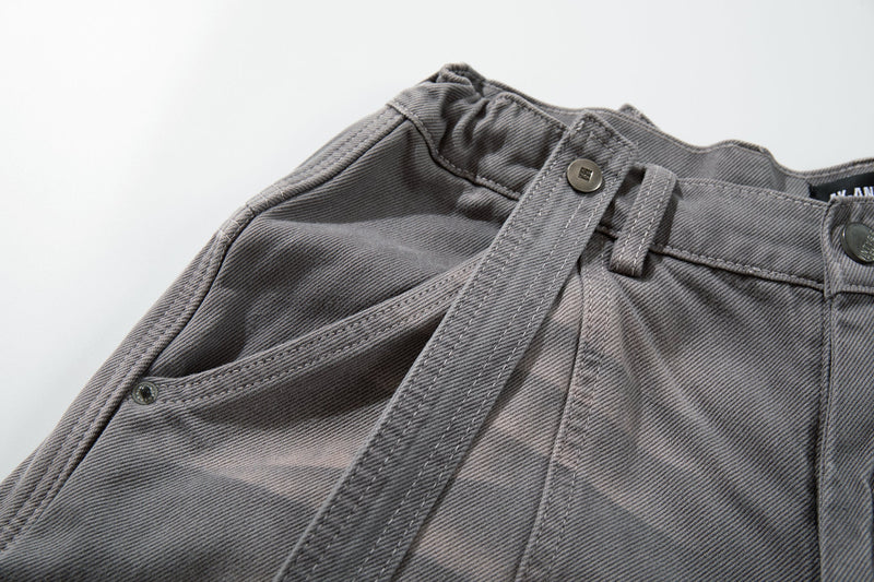 Close-up of gray jeans waistband corner with strap attachment and gathered fabric detail