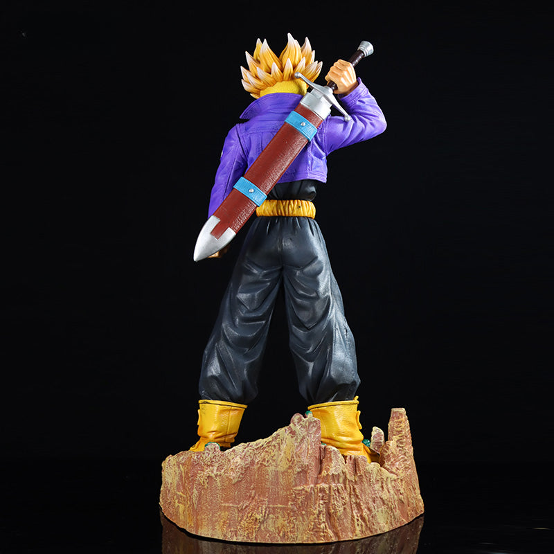 The Seakoff Trunks Collectible Figure from Dragon Ball Z stands 50cm tall on a rocky base, featuring interchangeable heads and a sword pose. This figure, with spiky blonde hair, a purple jacket, black pants, and yellow boots faces away against a black background.