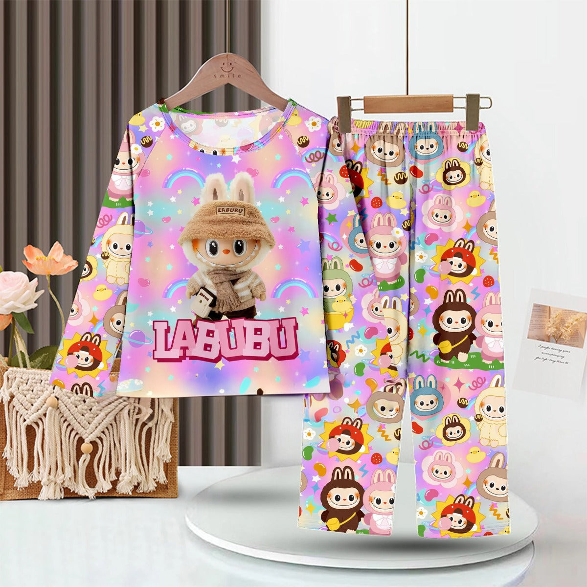 A colorful LABUBU Baby Pajama Set in soft milk silk hangs on a rack, showcasing a cartoon animal in a hat against a pastel rainbow. The long-sleeved top and pants are adorned with cheerful cartoon faces.