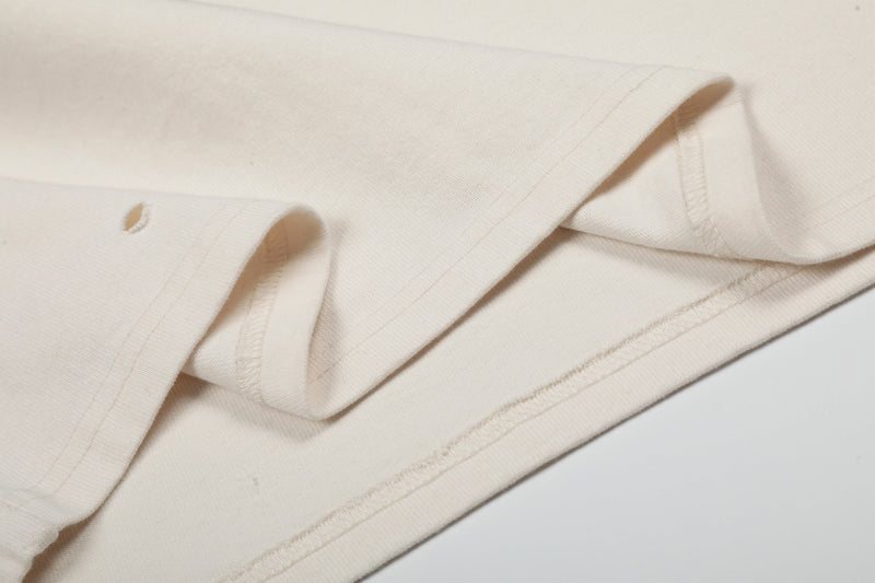 Close-up of an off-white distressed graphic band tee with rolled sleeves and visible seam details
