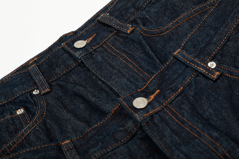 Close-up of the front waist on deep indigo jeans with snap button and angled seam details