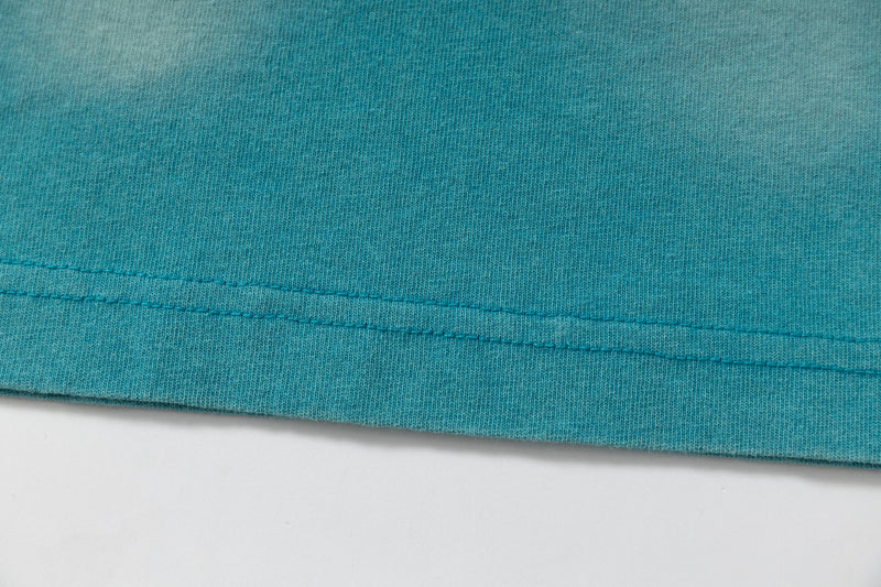 Close-up of a teal washed tee hem with visible stitching and soft vintage streetwear texture