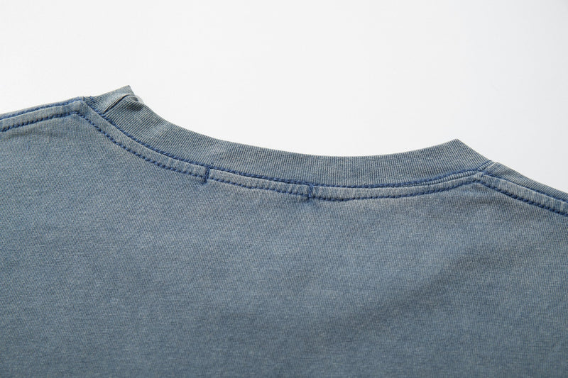 Close-up of a faded blue vintage washed graphic T-shirt with a ribbed crew neckline and visible seam stitching