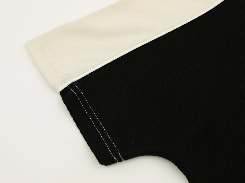 Close-up of a black and cream V-neck athletic tee with contrast stitching and curved hem detail