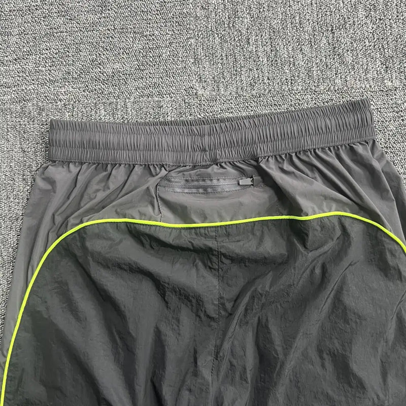A close-up of the waistband and upper section of gray athletic shorts with a neon yellow stripe, laid flat on a textured gray carpet—great for pairing with Syna World Black Yellow Logo Track Pants.
