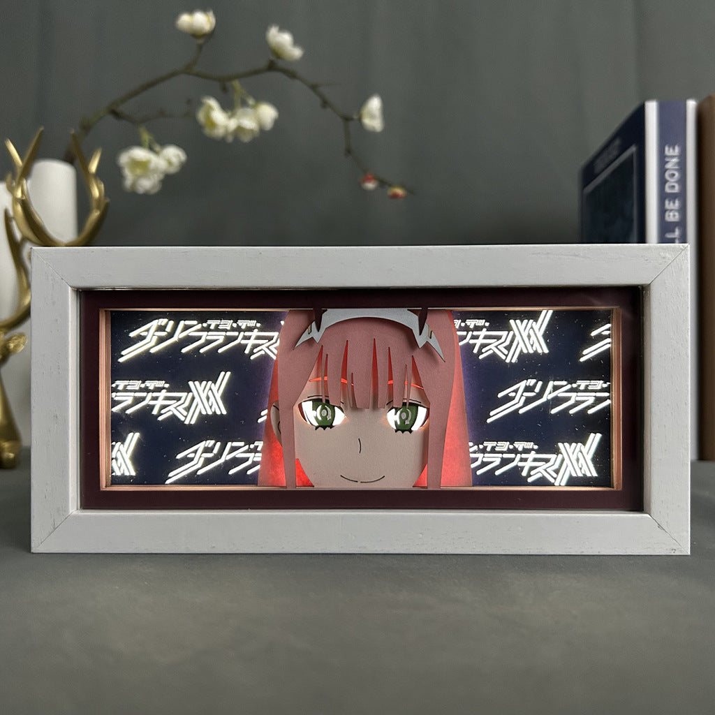 The Seakoff Darling in the Franxx Anime Light Box features a 3D effect of Zero Two with red hair and green eyes, set against repeating stylized text. It includes a 16-color adjustable LED light, with white-flowered branches and a book artfully positioned behind it for enhanced display.