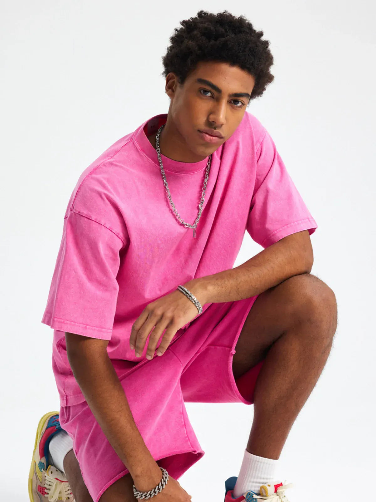 A young man poses against a plain white background in a Custom Anime Character Pink Washed T-Shirt - Personalized Anime Style Tee, matching shorts, chain necklace, bracelet, and colorful sneakers for a bold streetwear look.