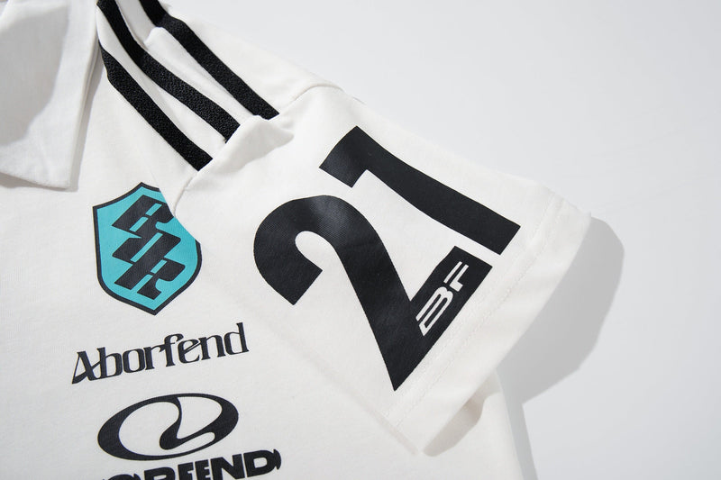 White racing crest polo shirt with black shoulder stripes and sponsor-style motorsport graphics on the chest and sleeve