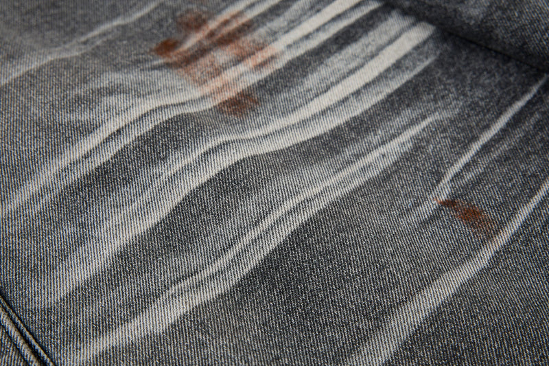 Close-up of gray denim fabric with wide white paint streaks and brown splatter