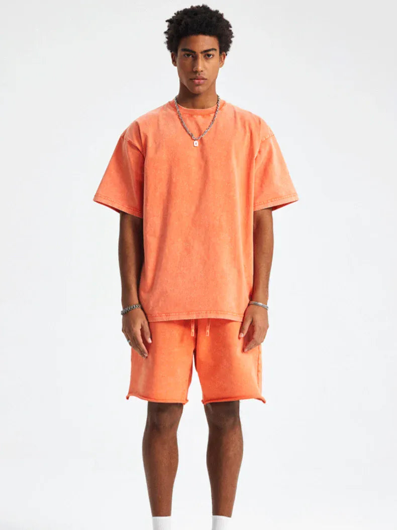 A man stands against a plain background wearing the Custom Anime Character Orange Washed T-Shirt - Personalized Anime Style Tee and matching orange shorts, paired with white socks and jewelry, looking directly at the camera.