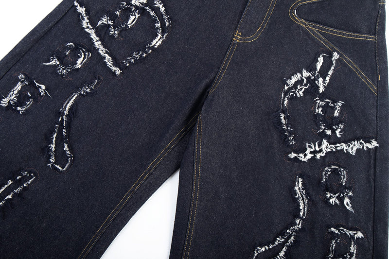 Close-up of distressed flame stitch details across the front legs of dark denim jeans