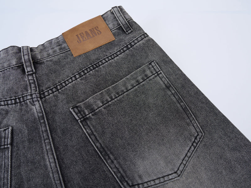 Back pocket close-up on grey washed denim jeans with brown JEANS label