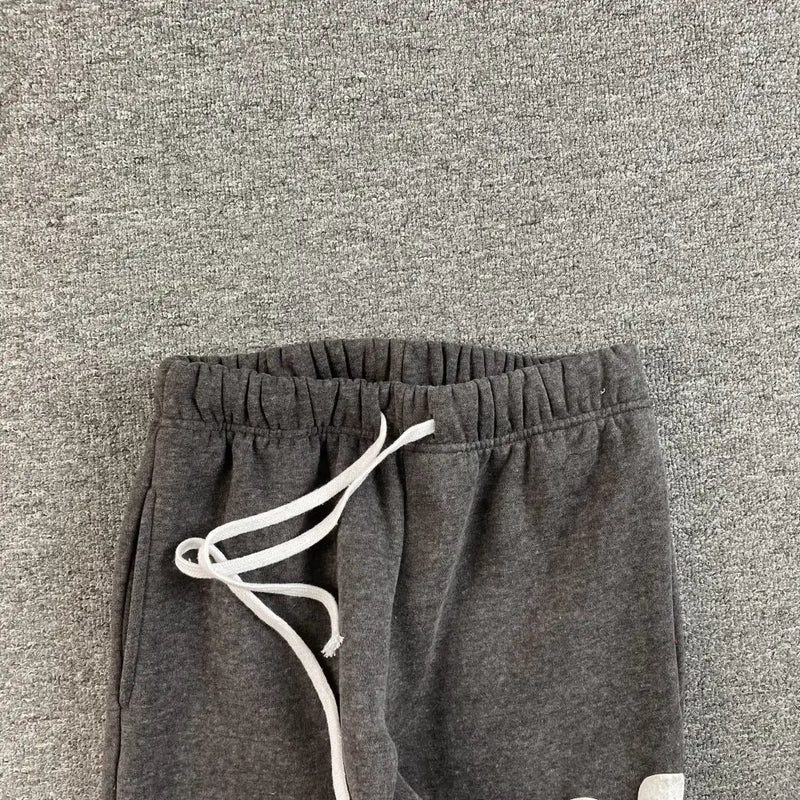 The waistband and upper part of the Syna World Dark Gray Graffiti Letter Print Jogger Pants, featuring white drawstrings, are shown lying on a matching gray textured surface.