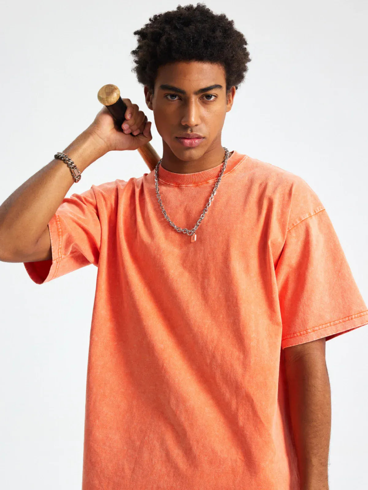 A young man wearing the Custom Anime Character Orange Washed T-Shirt stands against a plain background, holding a baseball bat over his shoulder and looking directly at the camera.