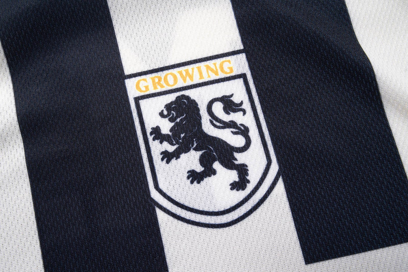 Black-and-white striped varsity soccer jersey with a lion crest and gold Growing emblem on textured fabric