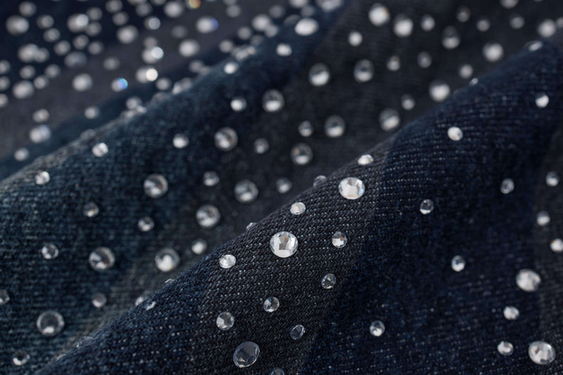 Close-up of dark wash denim fabric with scattered rhinestones