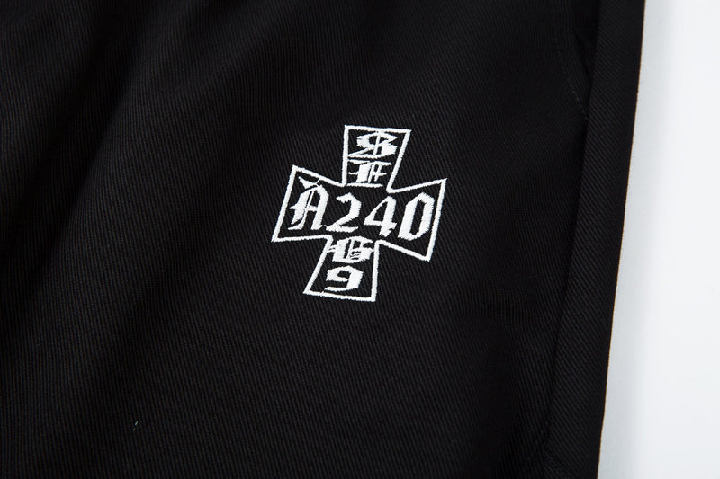 Close-up of white cross-shaped logo embroidery with numbers on black pants leg