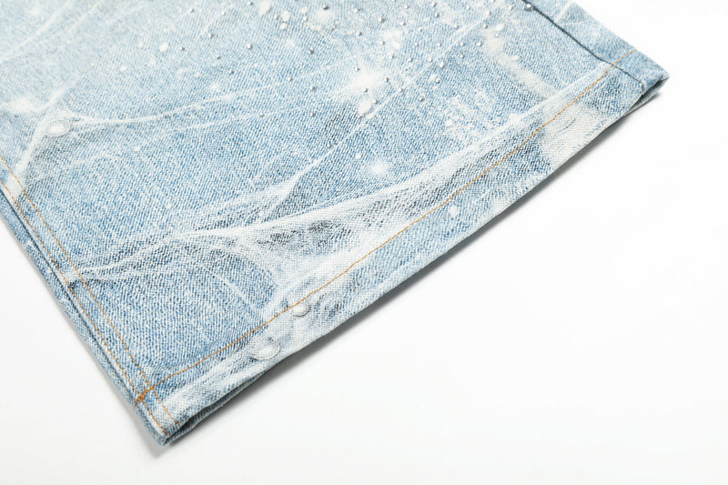 Cuffed hem of light blue wide-leg jeans with frosted spiderweb wash and orange stitching