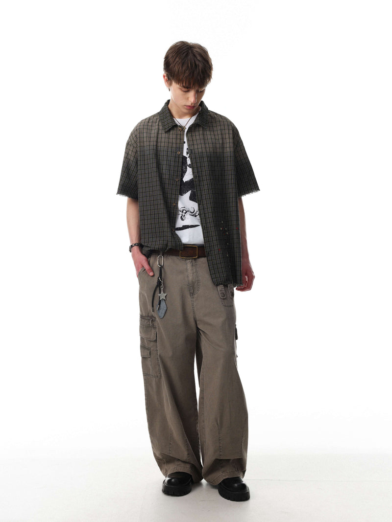 Model wearing a dark gradient plaid shirt with raw edges, layered over a graphic tee and cargo pants