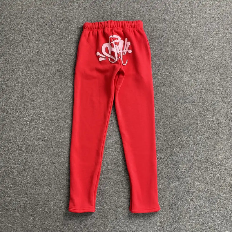 Syna World Red Script Embroidered Drawstring Jogger Pants laid flat on a gray surface, showcasing bold white script embroidery near the waistband—perfect statement streetwear joggers.