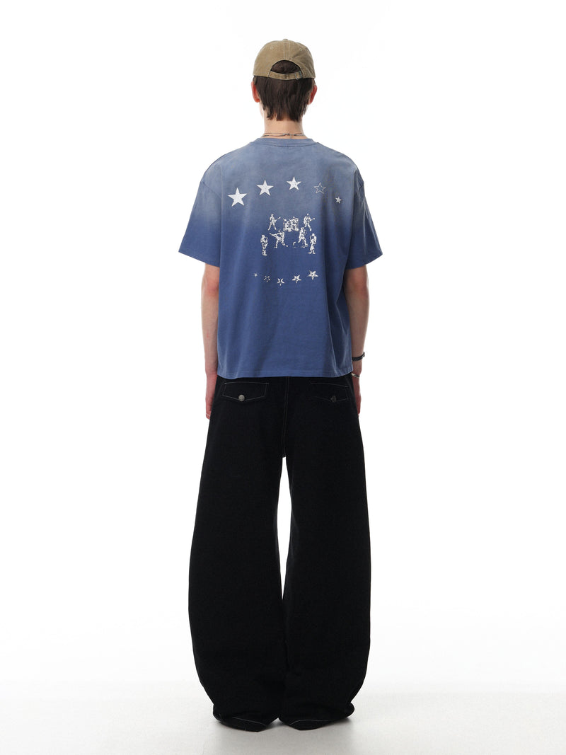 Back view of a blue gradient washed cotton tee with star graphics and faded graphic print, styled with black wide-leg pants and a cap