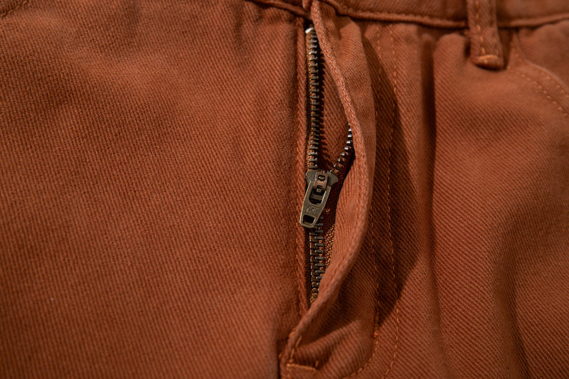 Close-up of the front fly on rust brown jeans with exposed zipper and top button area