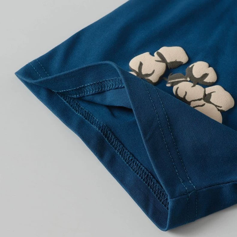 Close-up of the sleeve on the Denim Tears Blue Cotton Wreath Allover Print T-Shirt, showing three beige cotton flowers printed near the seam with visible fabric and stitching details.