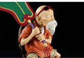 The Seakoff Master Roshi Collectible Figure features an elderly man with a white beard and sunglasses, seated on a brown turtle shell, wearing an orange shirt, and holding a large green Banana Fan. An ideal addition to any Dragon Ball collection, the stark black background enhances this unique 18cm figure&