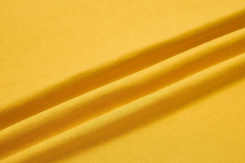 Close-up of bright yellow washed cotton tee fabric with soft draped folds and ribbed texture