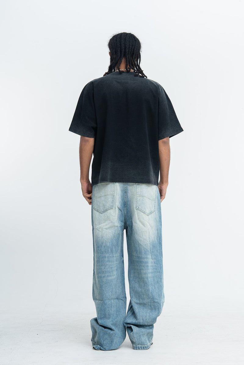 Back view of a black oversized vintage wash graphic tee paired with light blue baggy jeans in streetwear style