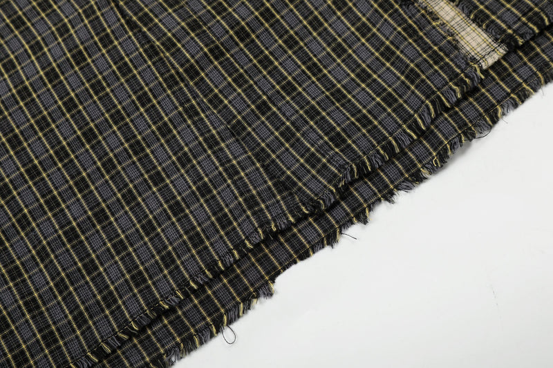 Close-up of black and yellow plaid fabric with distressed raw edges and frayed hem detail