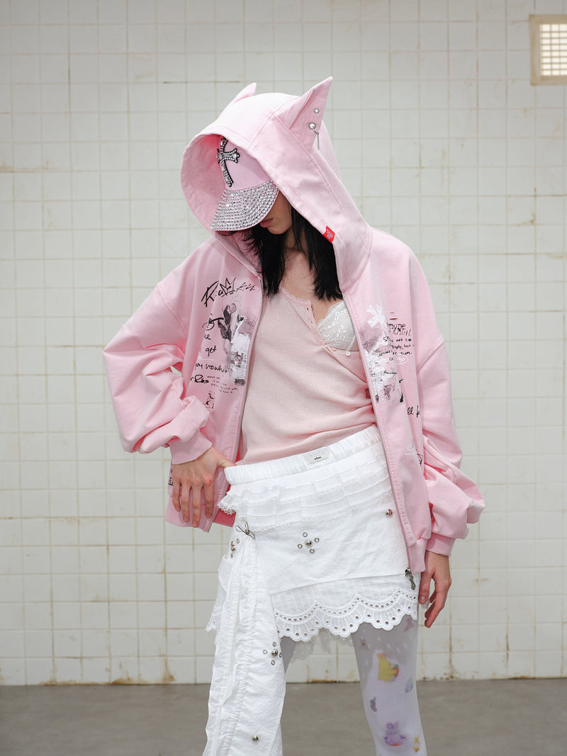 Model wearing pink graphic zip hoodie with hood up and matching cap