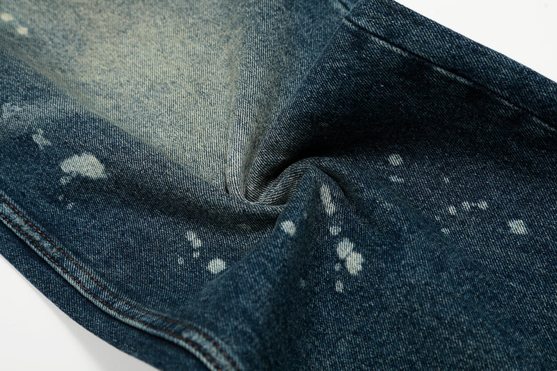 Close-up of blue denim fabric with white paint splatters and faded texture
