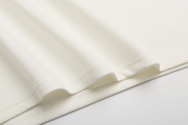 Close-up of creamy white textured polo shirt fabric with neat hem stitching and soft drape