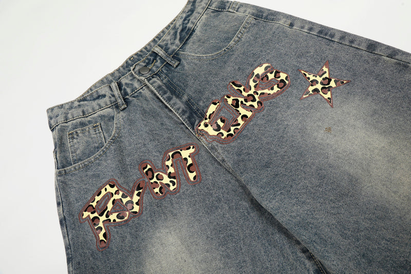 Rear angled view of wide-leg blue jeans with leopard word graphic and star patches