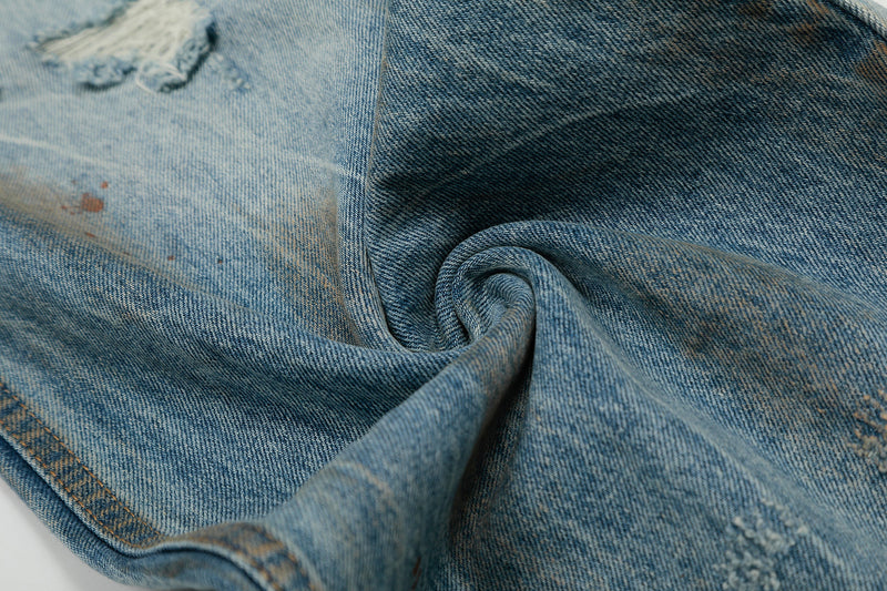 Close-up of folded distressed denim leg showing faded texture and rust-colored speckles