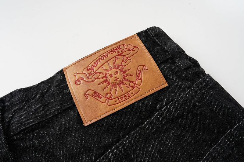 Tan leather back patch on black denim waistband with embossed sun design