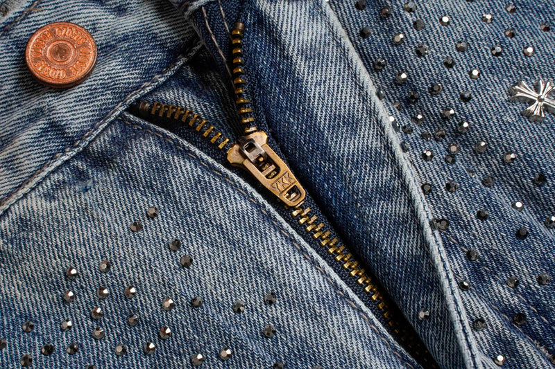 Close-up of light wash jeans fly with zipper, button, and rhinestones