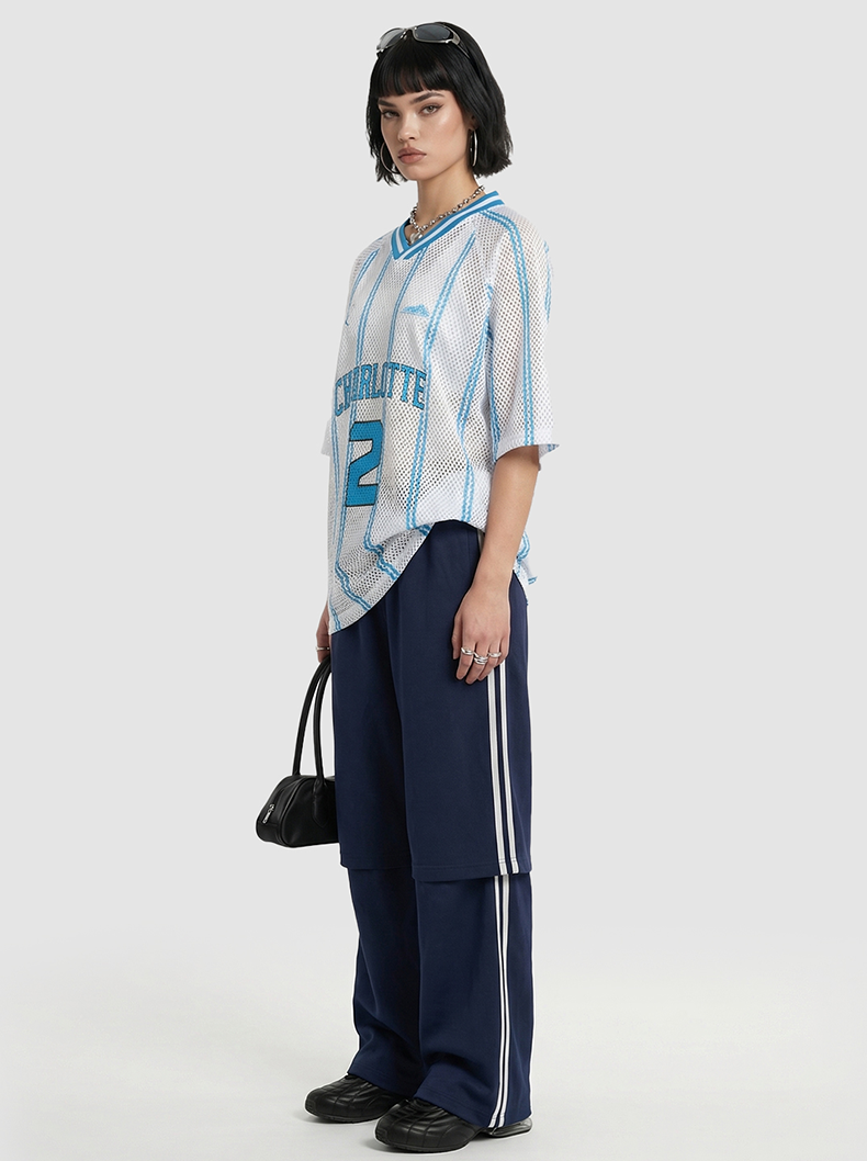 Model wearing a white mesh Charlotte Ball #2 jersey tee with blue trim, navy track pants, and black shoes against a white background