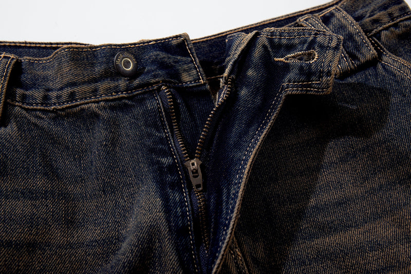 Close-up of the front fly on dark-wash jeans with zipper and waistband button