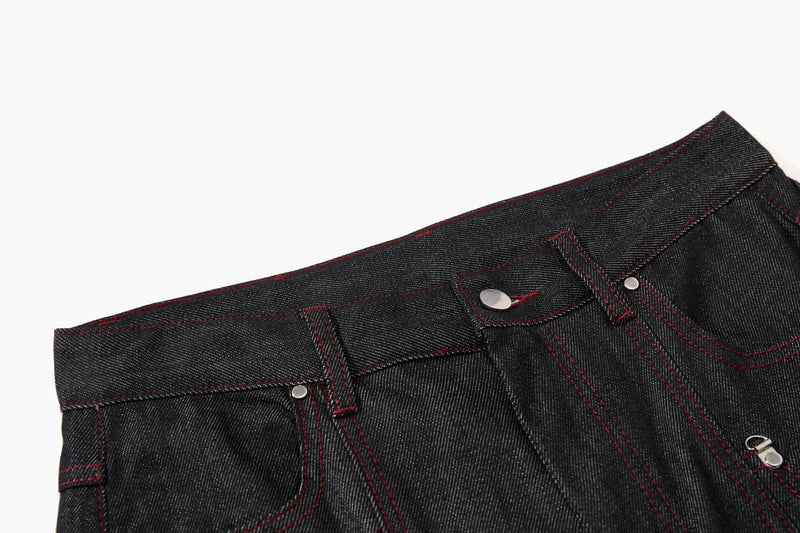 Close-up of black denim waistband with belt loops, silver button, and red contrast stitching