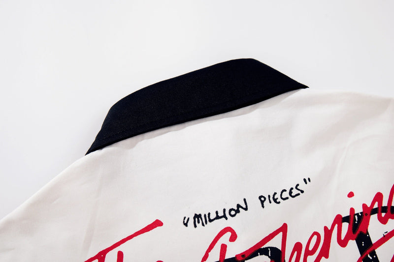Close-up of a white oversized graphic shirt with black collar and red handwritten-style print on the front