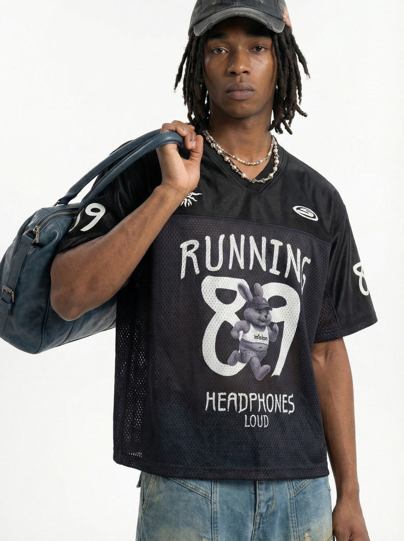 Model wearing a black mesh football jersey with Running 89 graphic, cap, beaded necklaces, and a navy duffel bag over shoulder