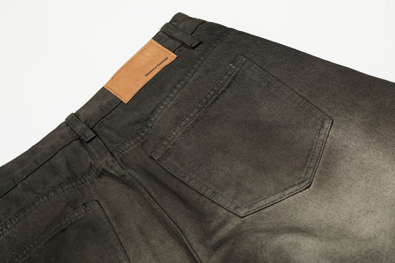 Close-up of back waistband and patch pocket on faded black denim pants with tan logo patch