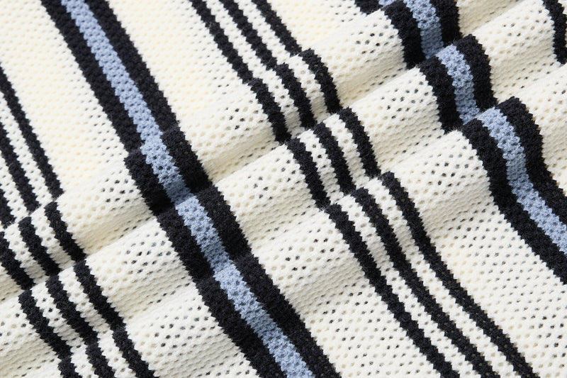 Close-up of cream knit polo fabric with black and light blue retro collegiate stripes and textured waffle knit detail