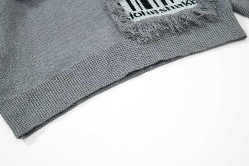 Gray knit sweater hem detail with ribbed edge and fringe patch visible above